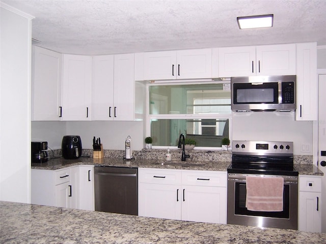 kitchen featuring sink, stone counters, appliances with stainless steel finishes, a textured ceiling, and white cabinets