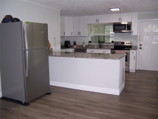 kitchen with dark wood-type flooring, white cabinetry, crown molding, dark stone countertops, and stainless steel appliances