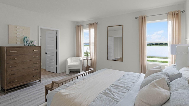 bedroom featuring multiple windows, a water view, and light wood-type flooring