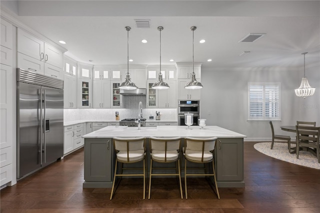 kitchen featuring appliances with stainless steel finishes, a kitchen island with sink, hanging light fixtures, white cabinetry, and tasteful backsplash