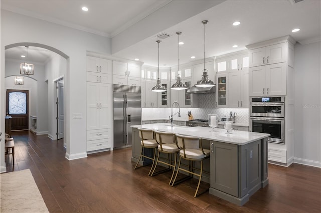 kitchen with stainless steel appliances, hanging light fixtures, a kitchen island with sink, and white cabinets