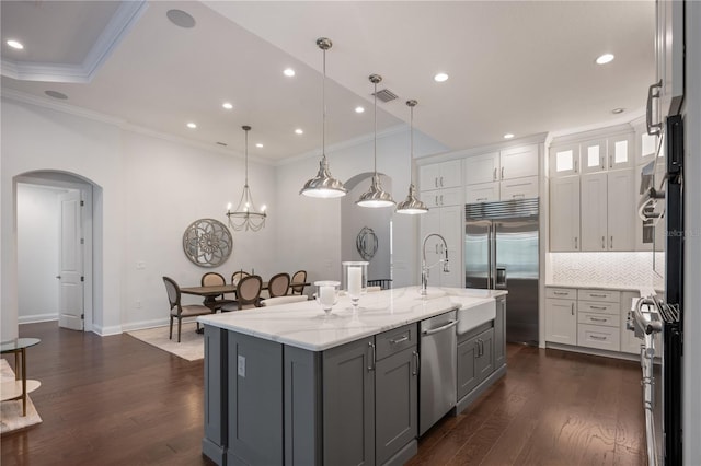 kitchen featuring appliances with stainless steel finishes, gray cabinetry, light stone counters, a center island with sink, and decorative light fixtures