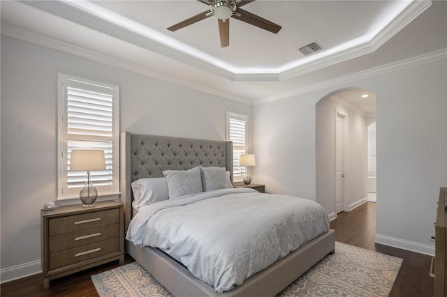 bedroom with crown molding, a tray ceiling, dark wood-type flooring, and ceiling fan