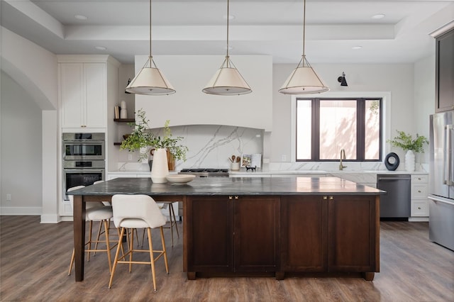 kitchen featuring hanging light fixtures, dark brown cabinets, a raised ceiling, and appliances with stainless steel finishes