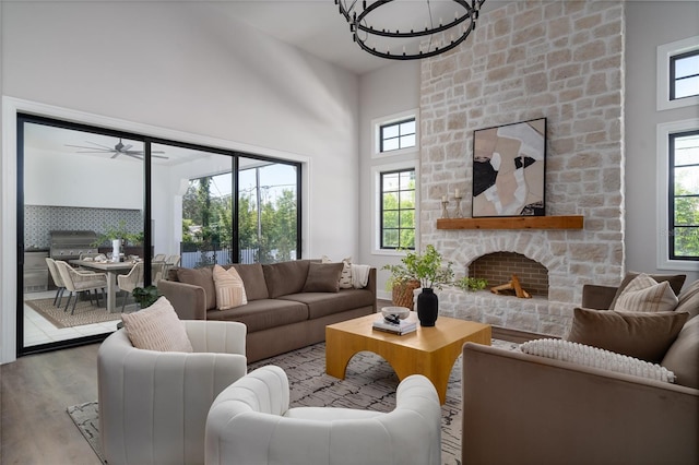 living room featuring a notable chandelier, a stone fireplace, wood-type flooring, and a towering ceiling