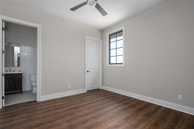 unfurnished bedroom featuring dark wood-type flooring, ensuite bathroom, sink, tile walls, and ceiling fan