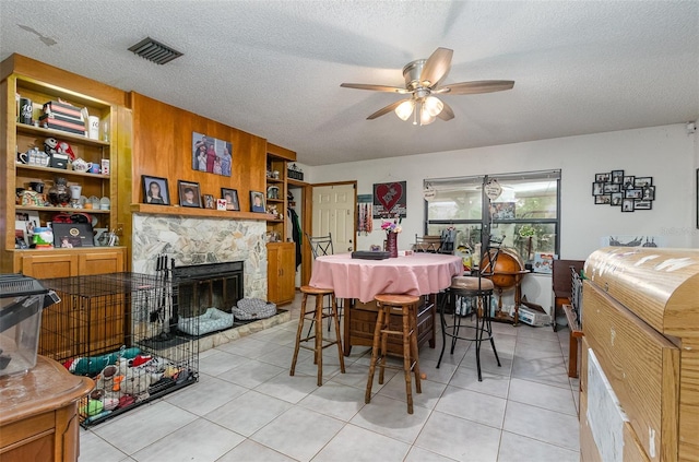 dining room with a textured ceiling, a stone fireplace, visible vents, and a ceiling fan