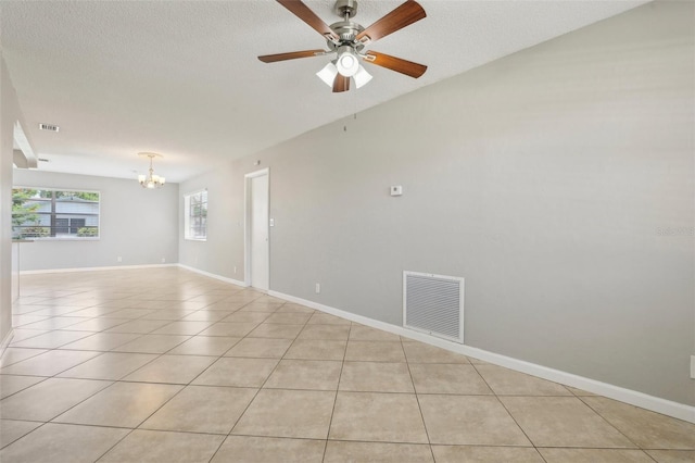 tiled empty room featuring ceiling fan with notable chandelier and a textured ceiling