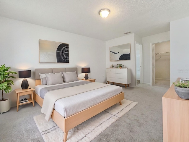 bedroom with a spacious closet, light carpet, and a textured ceiling