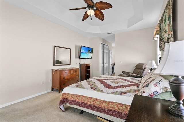 carpeted bedroom with ceiling fan, a raised ceiling, and a closet