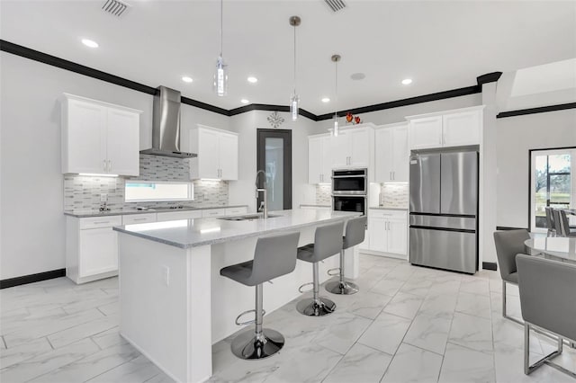 kitchen featuring decorative light fixtures, sink, a kitchen island with sink, stainless steel appliances, and wall chimney exhaust hood