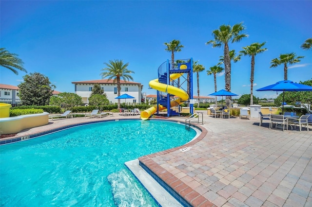 view of pool with a water slide, a playground, and a patio