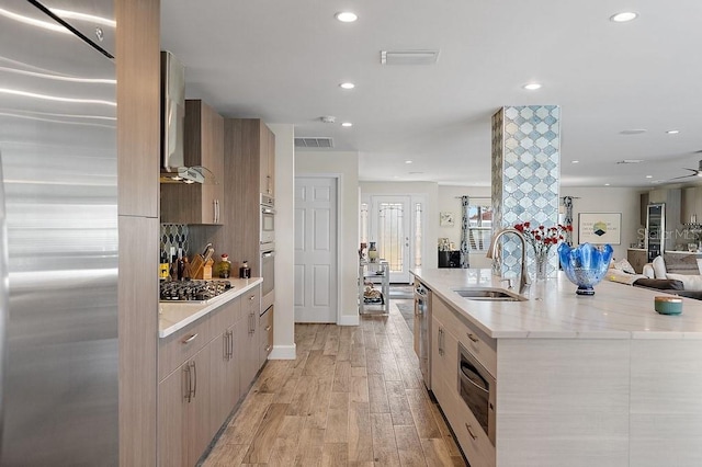 kitchen with sink, stainless steel appliances, a spacious island, light wood-type flooring, and light brown cabinets