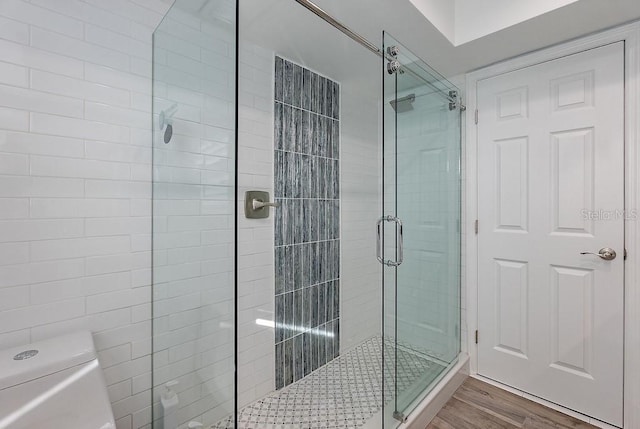 bathroom featuring hardwood / wood-style flooring, a shower with door, and toilet