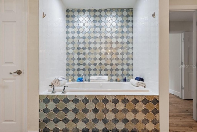 bathroom featuring a relaxing tiled tub and wood-type flooring