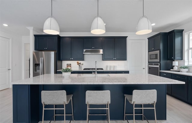 kitchen featuring light stone counters, decorative light fixtures, appliances with stainless steel finishes, and a center island with sink