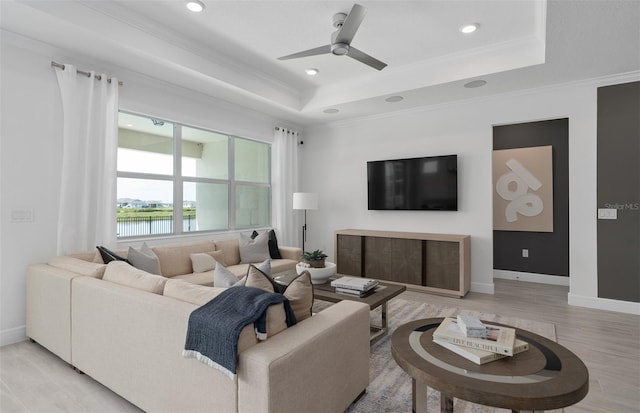 living room featuring crown molding, ceiling fan, a tray ceiling, and light wood-type flooring