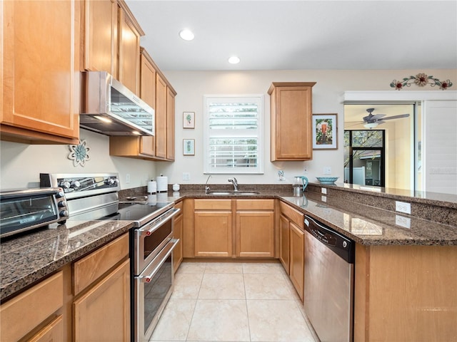 kitchen featuring appliances with stainless steel finishes, sink, dark stone counters, and range hood