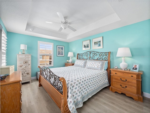 bedroom featuring ceiling fan, a tray ceiling, and light hardwood / wood-style flooring