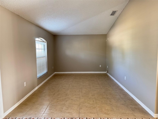 empty room with lofted ceiling, light tile patterned floors, and a textured ceiling