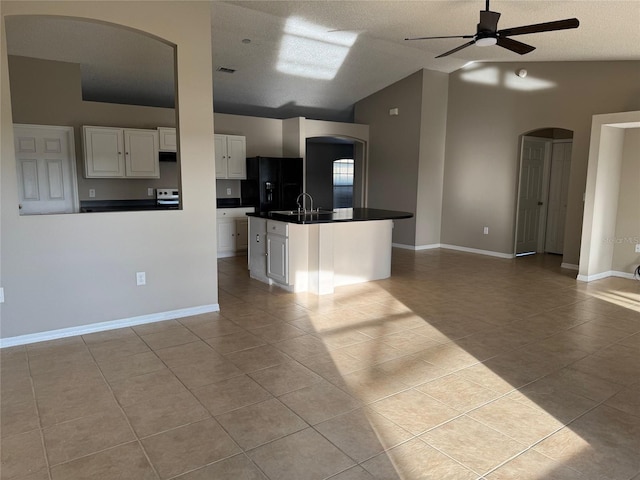 kitchen with ceiling fan, white cabinetry, a center island with sink, light tile patterned flooring, and black fridge