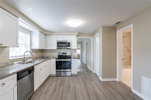 kitchen featuring white cabinetry, sink, stainless steel appliances, light stone countertops, and light wood-type flooring