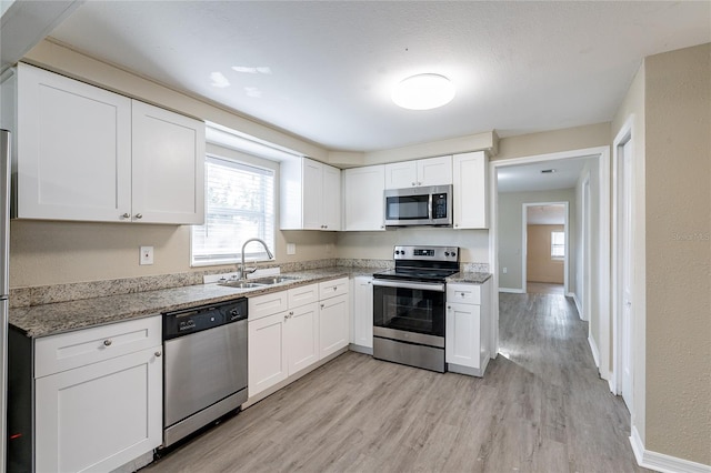 kitchen with stainless steel appliances, white cabinetry, light stone countertops, and sink