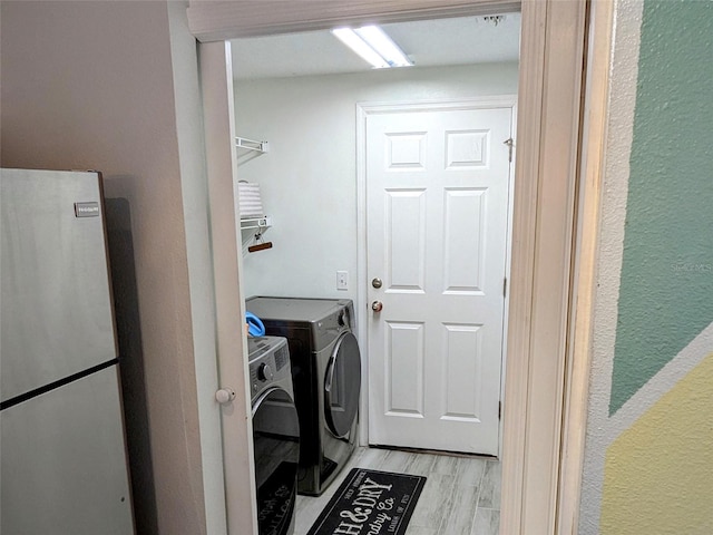 clothes washing area featuring washing machine and clothes dryer and light hardwood / wood-style flooring