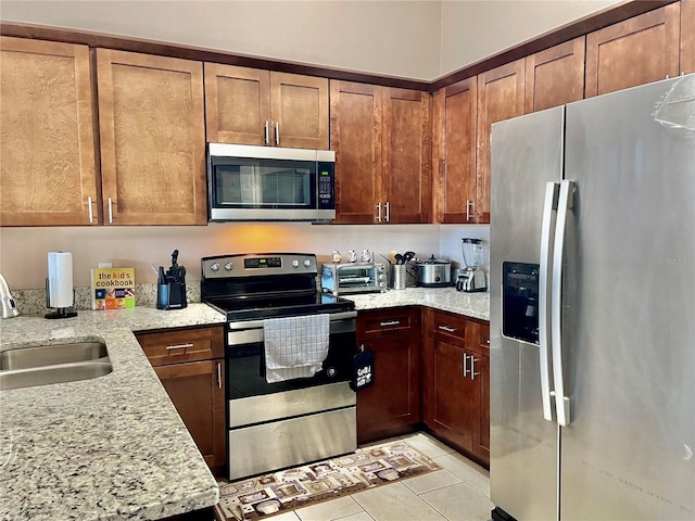 kitchen featuring light stone counters, sink, light tile patterned floors, and appliances with stainless steel finishes