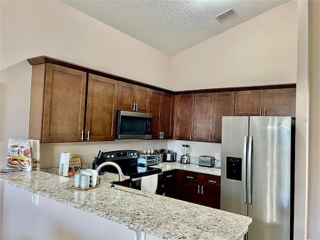 kitchen featuring lofted ceiling, light stone countertops, kitchen peninsula, and appliances with stainless steel finishes