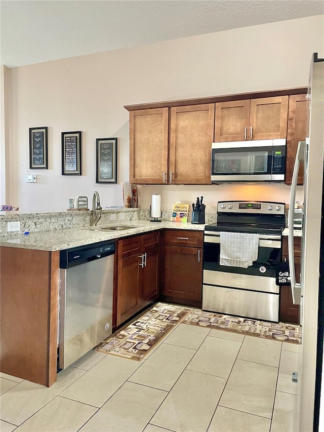 kitchen with light stone counters, stainless steel appliances, kitchen peninsula, and sink