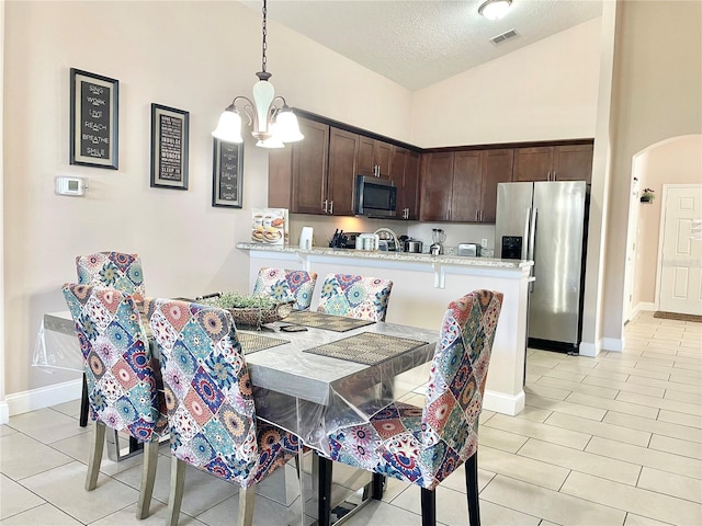 tiled dining area featuring high vaulted ceiling, a textured ceiling, and a notable chandelier