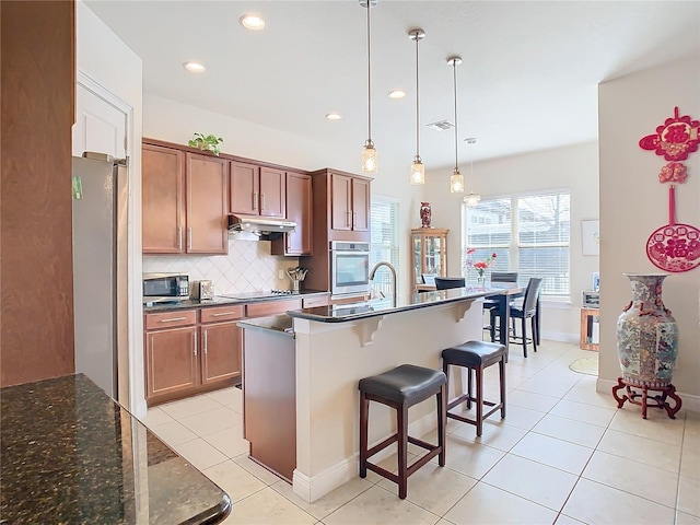 kitchen featuring a breakfast bar area, tasteful backsplash, light tile patterned floors, appliances with stainless steel finishes, and pendant lighting