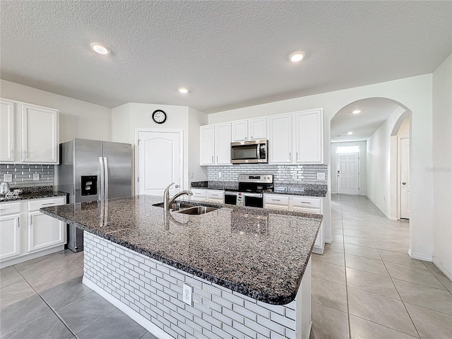 kitchen featuring light tile patterned flooring, appliances with stainless steel finishes, an island with sink, sink, and white cabinets