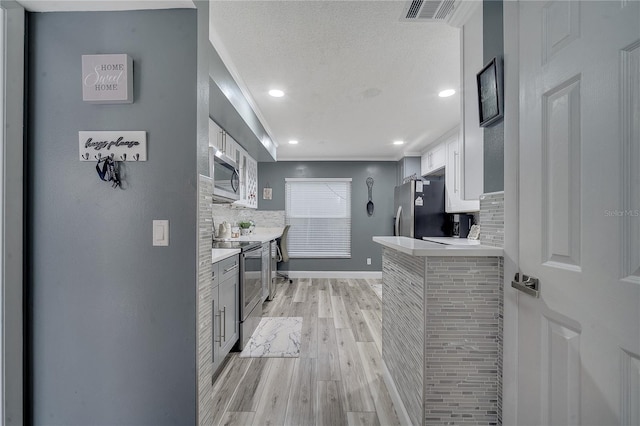 kitchen with appliances with stainless steel finishes, light wood-type flooring, white cabinets, decorative backsplash, and a textured ceiling