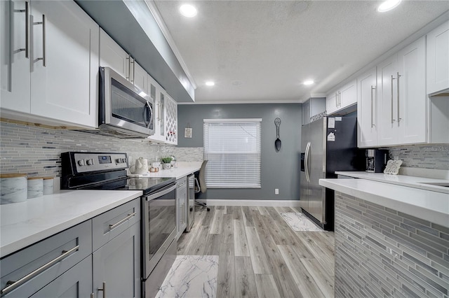 kitchen featuring crown molding, white cabinets, stainless steel appliances, light hardwood / wood-style floors, and backsplash