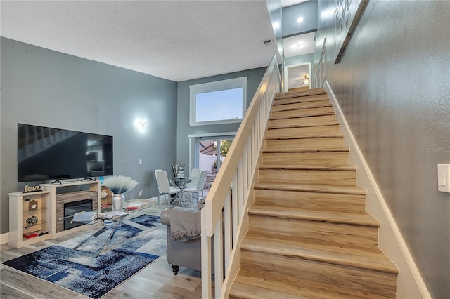 stairway with a high ceiling, a stone fireplace, hardwood / wood-style floors, and a textured ceiling