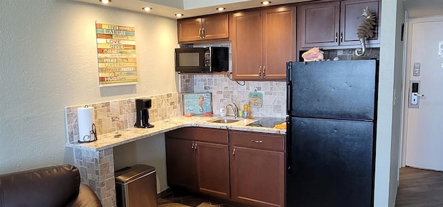 kitchen with light stone counters, a sink, black appliances, tasteful backsplash, and dark wood finished floors