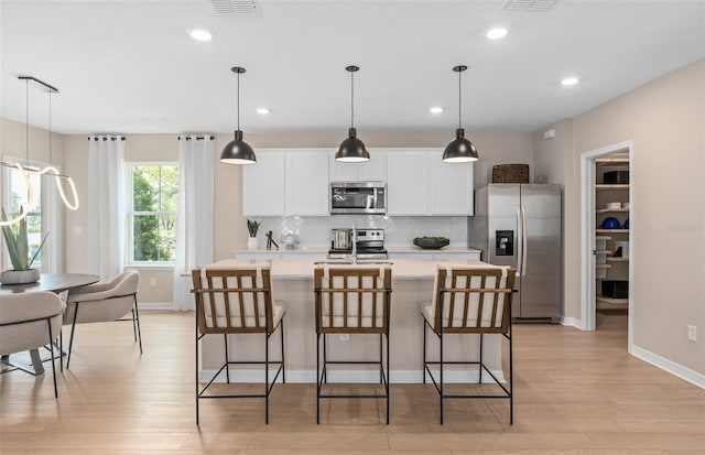 kitchen featuring decorative light fixtures, tasteful backsplash, an island with sink, white cabinetry, and stainless steel appliances