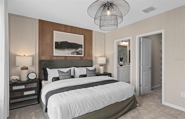 bedroom with an inviting chandelier, ensuite bath, and light colored carpet