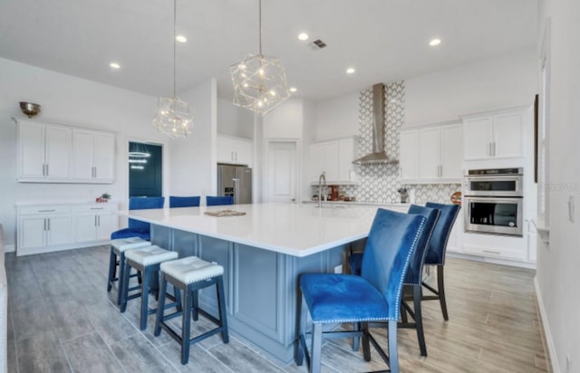 kitchen featuring pendant lighting, white cabinetry, wall chimney exhaust hood, stainless steel appliances, and a spacious island