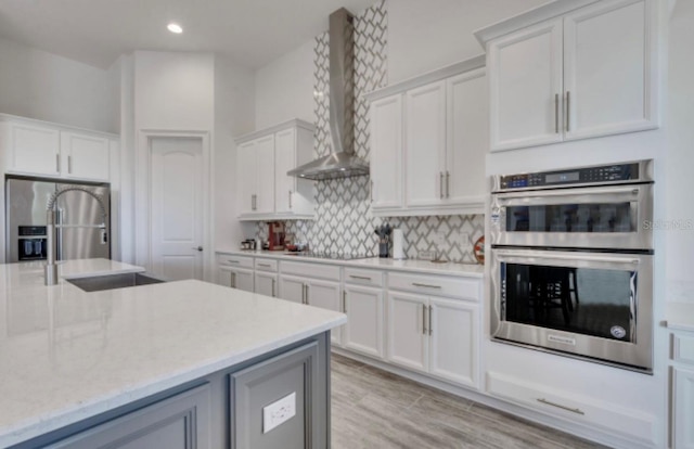 kitchen featuring wall chimney range hood, sink, appliances with stainless steel finishes, white cabinets, and decorative backsplash