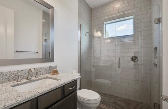 bathroom featuring vanity, a shower with shower door, and toilet