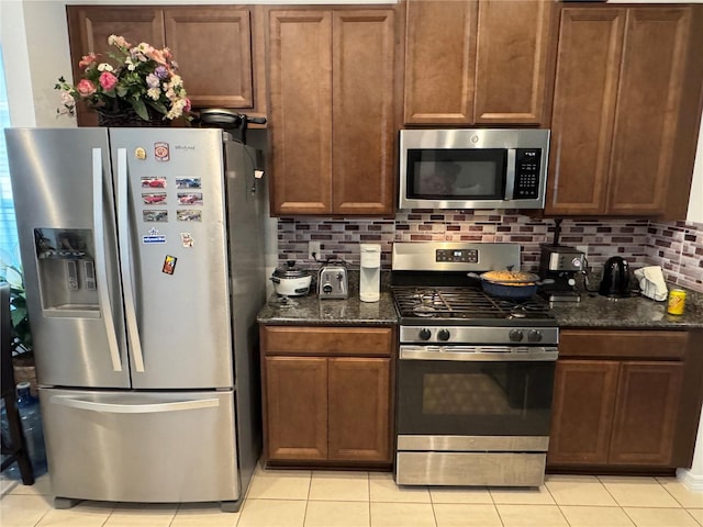 kitchen featuring stainless steel appliances, tasteful backsplash, dark stone countertops, and light tile patterned flooring