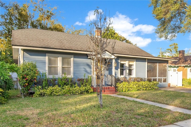 view of front of house featuring a front yard, a sunroom, roof with shingles, and a chimney