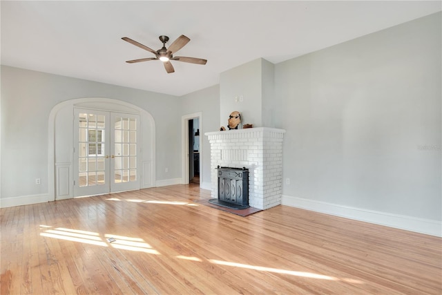 unfurnished living room with ceiling fan, a brick fireplace, light wood-type flooring, and french doors