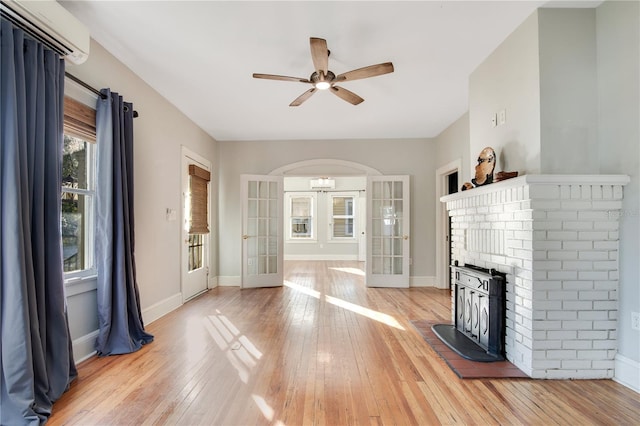 unfurnished living room featuring french doors, a wall mounted air conditioner, hardwood / wood-style flooring, ceiling fan, and a fireplace