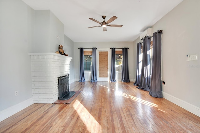 unfurnished living room featuring baseboards, a wall unit AC, light wood-style flooring, and a ceiling fan