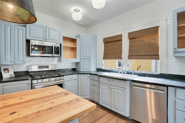 kitchen featuring sink, tasteful backsplash, light wood-type flooring, gray cabinets, and stainless steel appliances