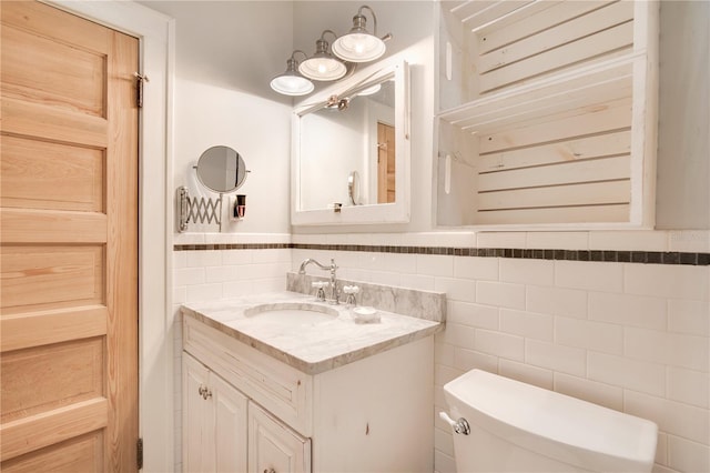 bathroom with toilet, wainscoting, tile walls, and vanity